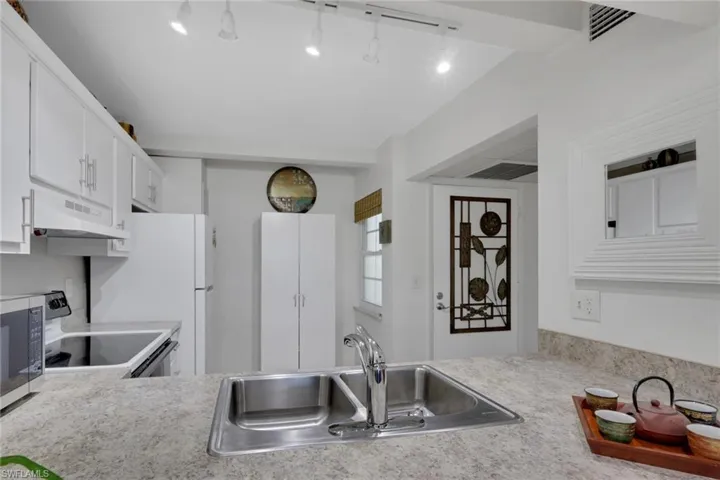 Kitchen with light countertops, electric stove, stainless steel microwave, under cabinet range hood, and white cabinets