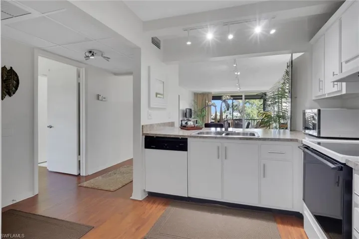 Kitchen with white cabinetry, light countertops, white appliances, and light wood-style floors