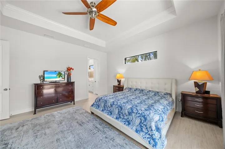 Bedroom with a tray ceiling, wood finished floors, crown molding, ensuite bath, and a ceiling fan
