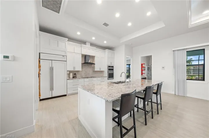 Kitchen with recessed lighting, a large island, white cabinets, a kitchen breakfast bar, and tasteful backsplash
