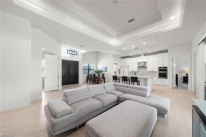 Living area featuring a raised ceiling, light wood-type flooring, ornamental molding, and recessed lighting