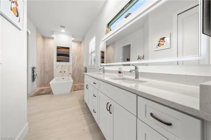 Bathroom with double vanity, a freestanding tub, recessed lighting, and wood finished floors