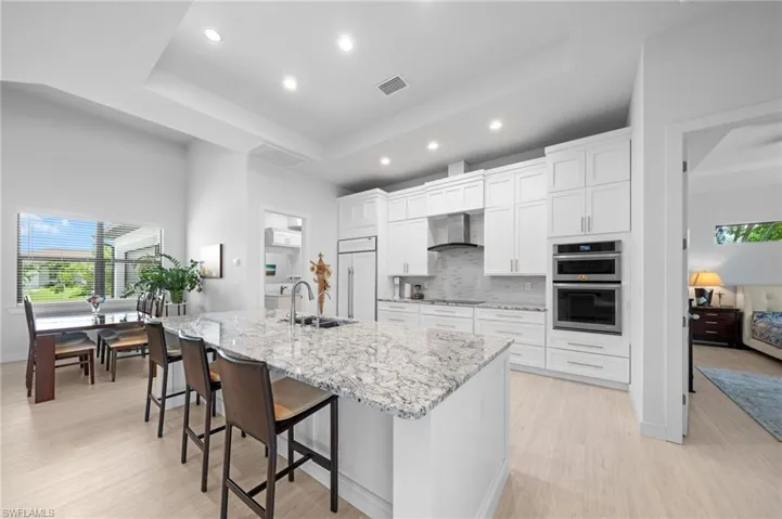 Kitchen with backsplash, a raised ceiling, recessed lighting, a spacious island, and white cabinetry