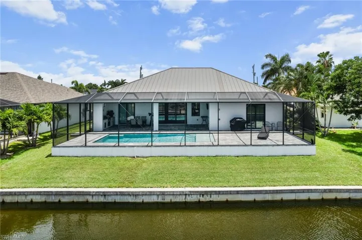 Back of house with a water view, a patio, and a lawn