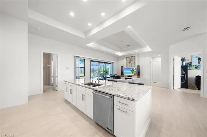 Kitchen featuring a center island with sink, a raised ceiling, light wood-type flooring, stainless steel dishwasher, and recessed lighting