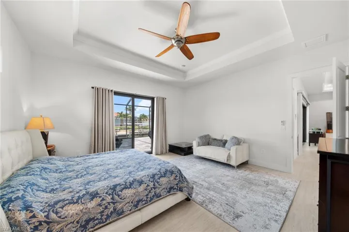 Bedroom featuring a raised ceiling, access to exterior, wood finished floors, a ceiling fan, and crown molding