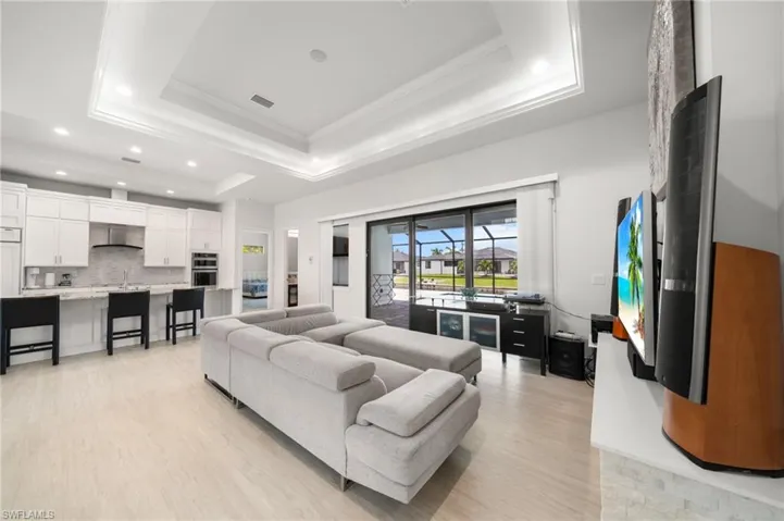 Living area with ornamental molding, a tray ceiling, light wood-style floors, and recessed lighting