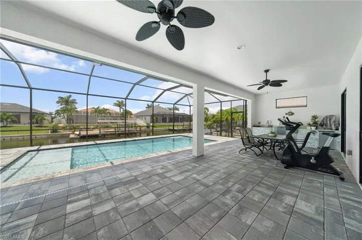 Outdoor pool featuring a ceiling fan, a patio, a water view, and glass enclosure