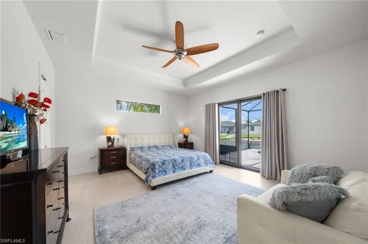Bedroom featuring access to outside, a tray ceiling, light wood-style floors, and a ceiling fan