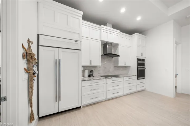 Kitchen with paneled built in fridge, decorative backsplash, light wood finished floors, white cabinets, and recessed lighting