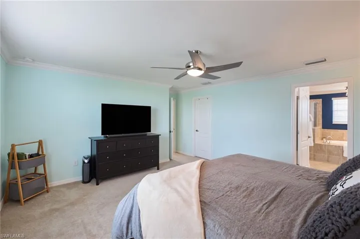 Carpeted bedroom with ceiling fan, ornamental molding, and connected bathroom