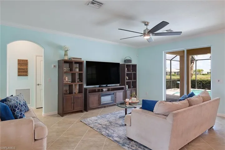 Living room featuring ceiling fan, light tile patterned floors, and crown molding