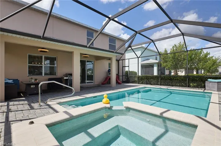 View of swimming pool featuring glass enclosure, grilling area, a patio, and an in ground hot tub