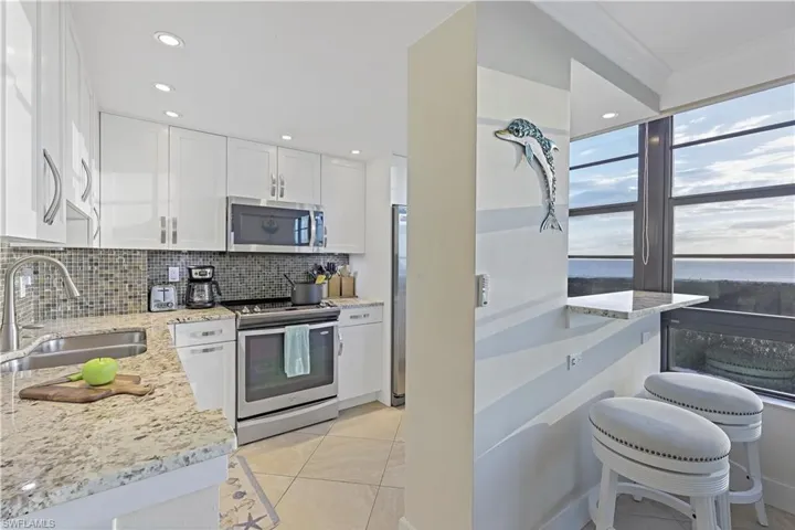 Kitchen featuring sink, white cabinetry, stainless steel appliances, light stone counters, and tasteful backsplash