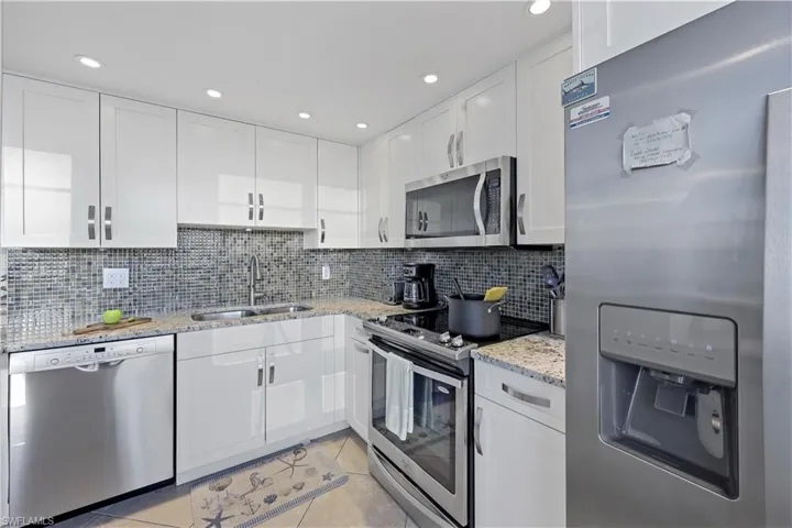 Kitchen with appliances with stainless steel finishes, sink, white cabinets, decorative backsplash, and light tile patterned floors