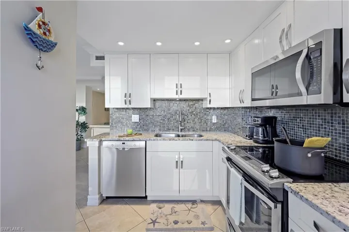 Kitchen with white cabinetry, appliances with stainless steel finishes, sink, and light stone counters