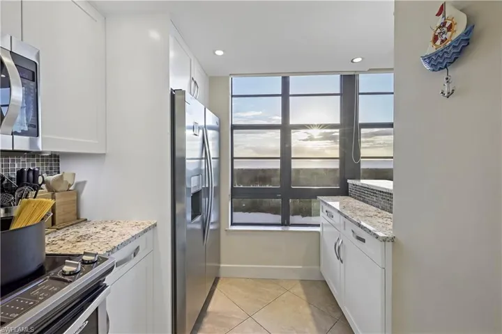 Kitchen with tasteful backsplash, light stone countertops, stainless steel appliances, and white cabinets