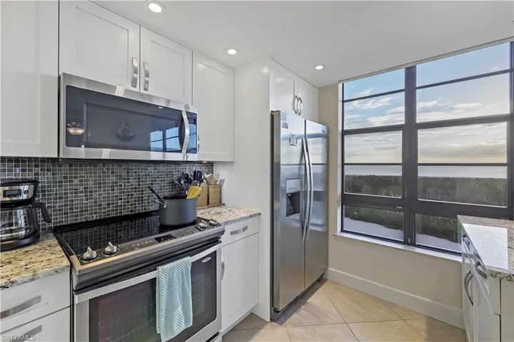 Kitchen with stainless steel appliances, white cabinets, and light stone counters