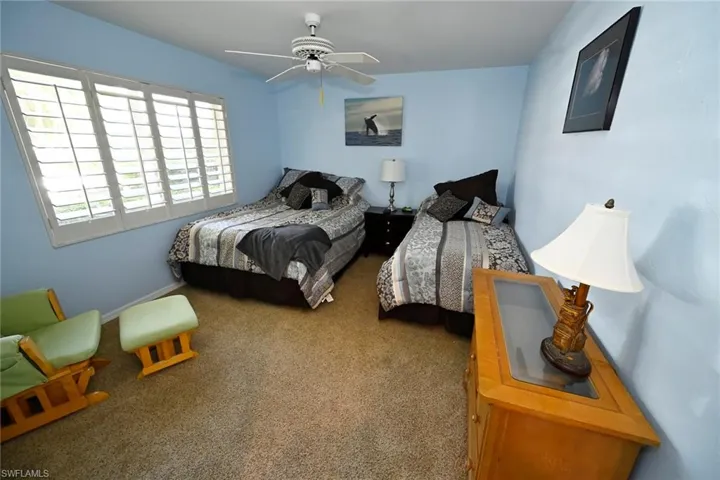 Carpeted bedroom with ceiling fan, plantation shutters.