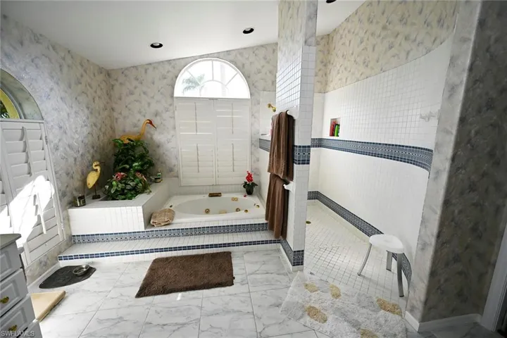 Bathroom with a tub with jets, marble finish floor, a walk in shower, and dual sinks.