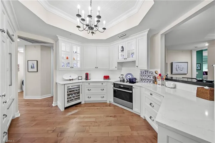 Kitchen with pendant lighting, beverage cooler, white cabinets, oven, and crown molding