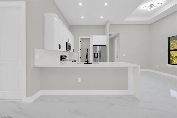 Kitchen with light marble finish floors, a peninsula, stainless steel appliances, white cabinetry, and recessed lighting