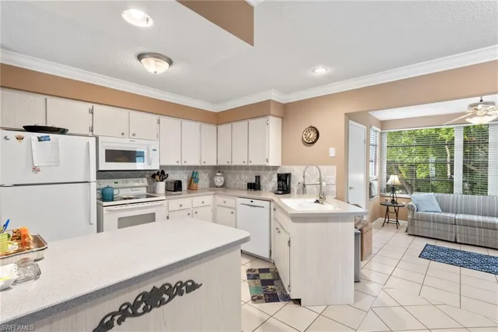 Kitchen with white cabinets, sink, backsplash, and white appliances