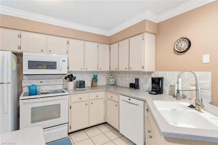 Kitchen featuring crown molding, tasteful backsplash, white appliances, and light tile patterned floors