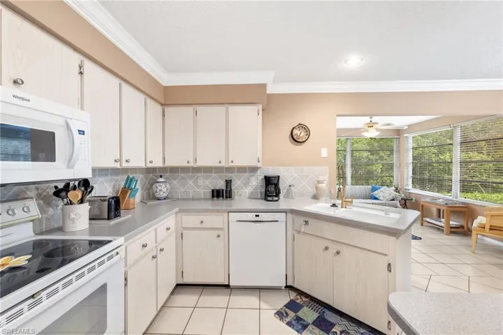 Kitchen with white appliances, light tile patterned floors, ceiling fan, tasteful backsplash, and kitchen peninsula