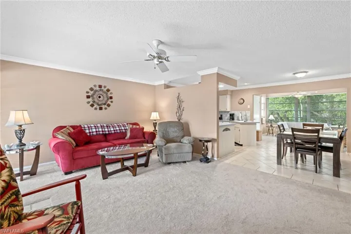 Living room with ceiling fan, a textured ceiling, light carpet, and crown molding
