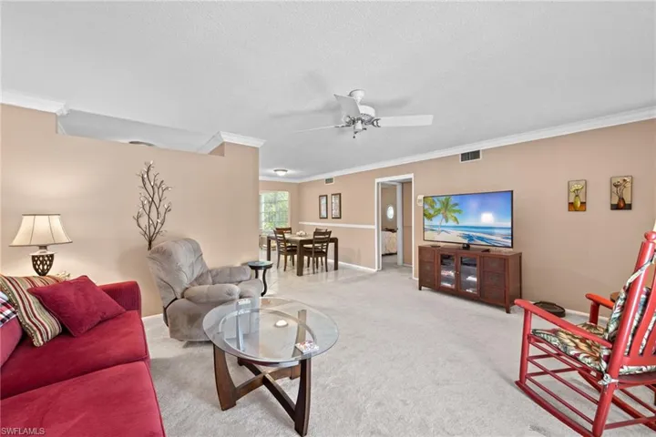 Carpeted living room with ceiling fan, crown molding, and a textured ceiling