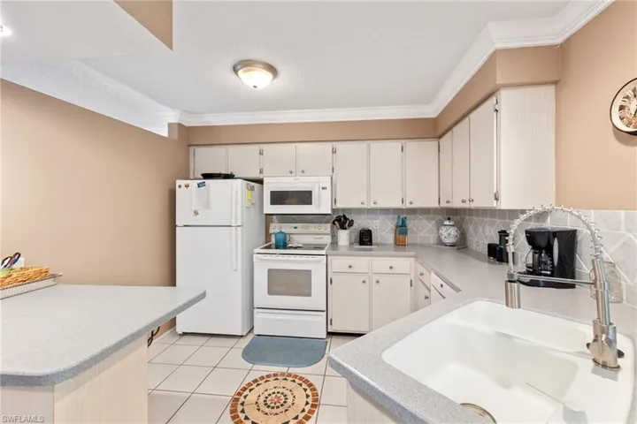 Kitchen featuring decorative backsplash, light tile patterned flooring, ornamental molding, white appliances, and sink