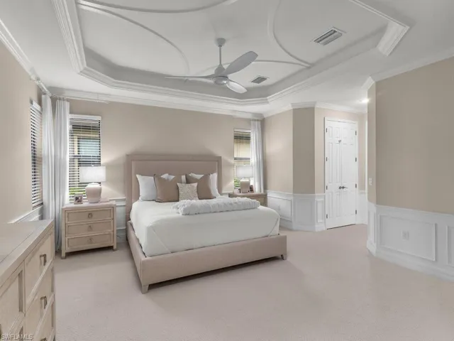 Bedroom with a raised ceiling, a closet, ceiling fan, ornamental molding, and light carpet