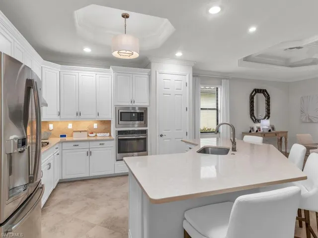 Kitchen with stainless steel appliances, white cabinetry, a raised ceiling, and crown molding