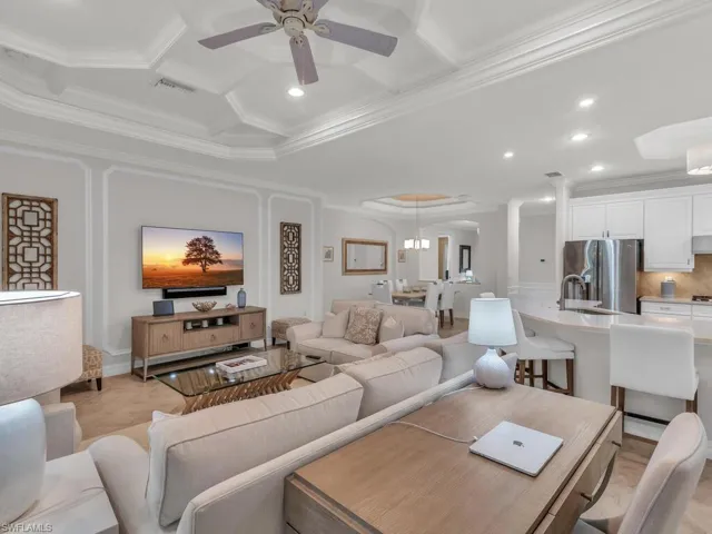 Living room with ceiling fan with notable chandelier, ornamental molding, coffered ceiling, and sink