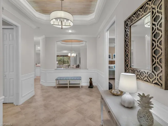 Corridor with wooden ceiling, a raised ceiling, an inviting chandelier, and crown molding