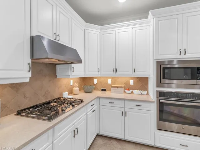 Kitchen with white cabinets, stainless steel appliances, decorative backsplash, and light tile patterned floors