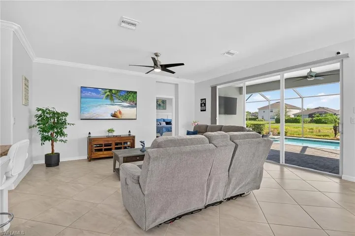 Living room featuring a sunroom, a ceiling fan, ornamental molding, and light tile patterned floors