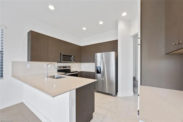 Kitchen with a peninsula, a sink, stainless steel appliances, light countertops, and dark brown cabinetry