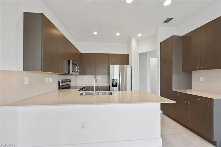 Kitchen featuring visible vents, a peninsula, a sink, stainless steel appliances, and dark brown cabinetry