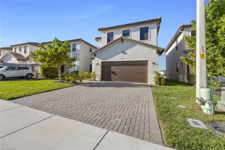 View of front of property featuring a front yard, decorative driveway, a tile roof, and stucco siding
