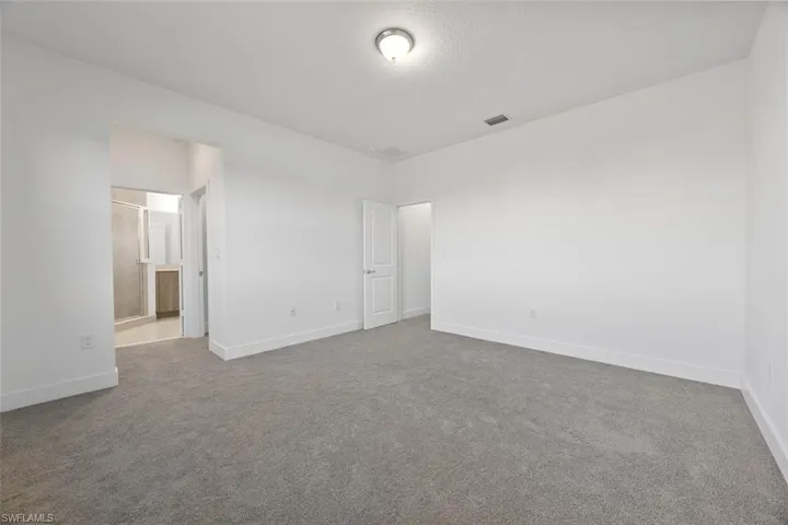 Unfurnished bedroom featuring visible vents, connected bathroom, baseboards, carpet flooring, and a textured ceiling