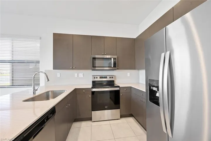 Kitchen with a sink, stainless steel appliances, light tile patterned flooring, light countertops, and dark brown cabinets