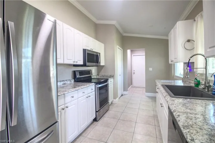 Kitchen featuring light stone countertops, appliances with stainless steel finishes, white cabinetry, and sink
