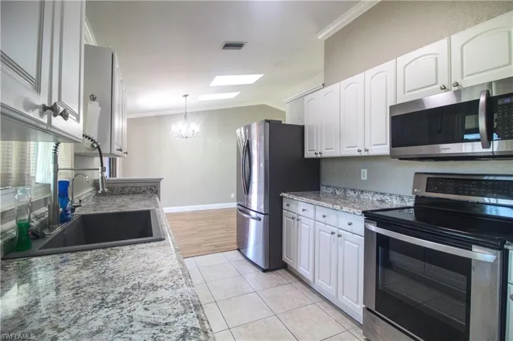 Kitchen with light stone countertops, appliances with stainless steel finishes, crown molding, sink, and white cabinets