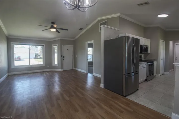 Kitchen featuring stainless steel appliances, crown molding, vaulted ceiling, white cabinets, and ceiling fan with notable chandelier