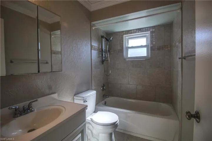 Guest bathroom with tiled shower / bath combo, tile patterned floors, toilet, vanity, and ornamental molding