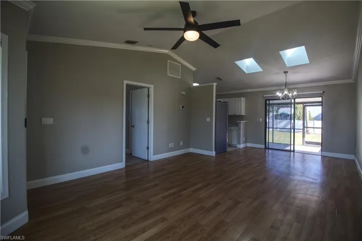 Unfurnished living room featuring lofted ceiling with skylight, crown molding, dark hardwood / wood-style floors, and ceiling fan with notable chandelier