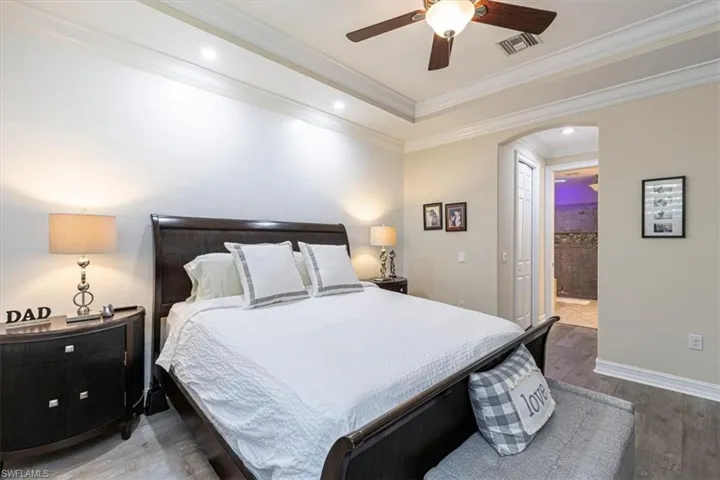 Bedroom with arched walkways, ensuite bathroom, wood finished floors, ceiling fan, and recessed lighting