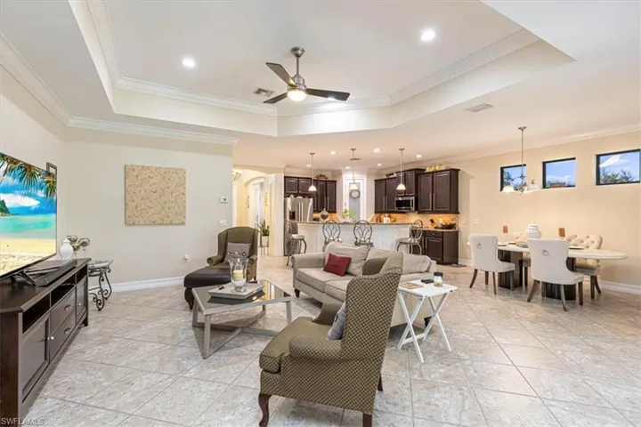 Living area featuring a tray ceiling, ceiling fan, crown molding, recessed lighting, and light tile patterned floors